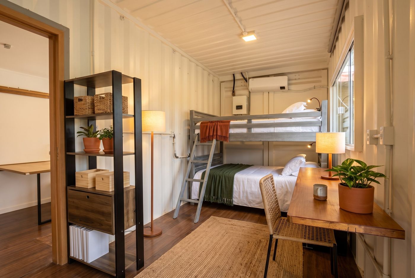 A sala-quarto com o beliche: roupa de cama branca, uma manta de cor em cada cama, uma luz para cada lugar de dormir e a chapa clara sem nada preso. Imagem conceitual gerada por IA.