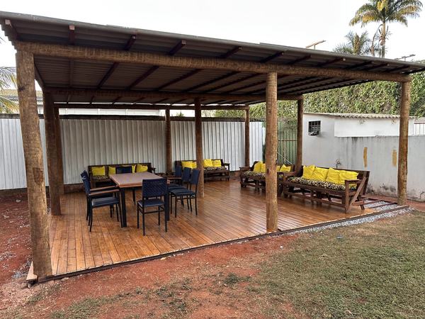 Pergolado de madeira com deck, mesa e sofás