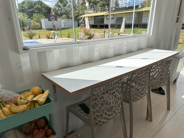 Mesa comunitária junto à janela, com vista para o gramado e a piscina