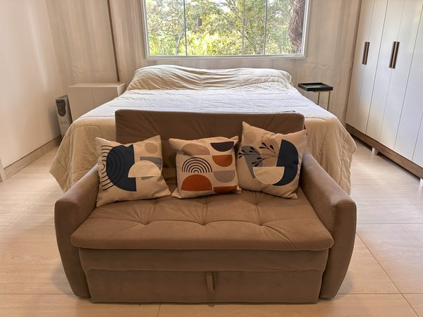 Quarto com cama de casal, sofá e janela para o verde