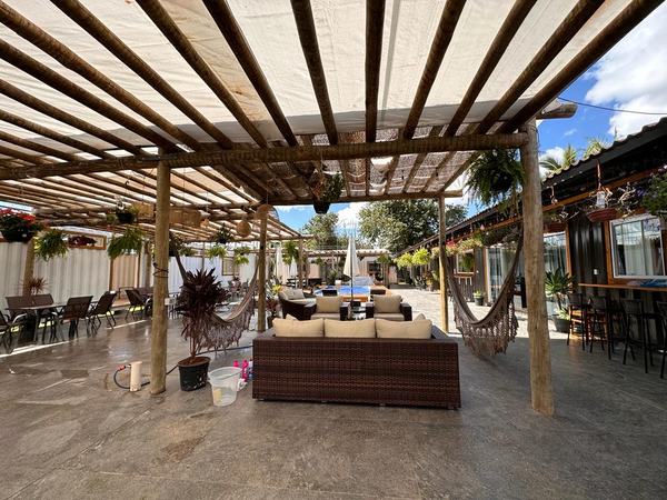 Lounge sob o pergolado, com sofás e a piscina ao fundo