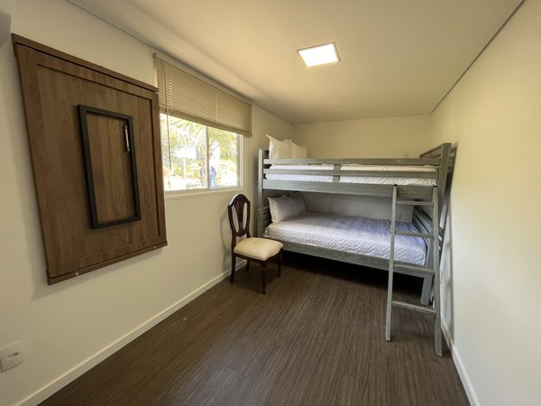 Quarto com beliche, cadeira de apoio e janela ampla