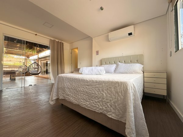 Suíte com cama de casal, ar-condicionado e parede de vidro para a área externa
