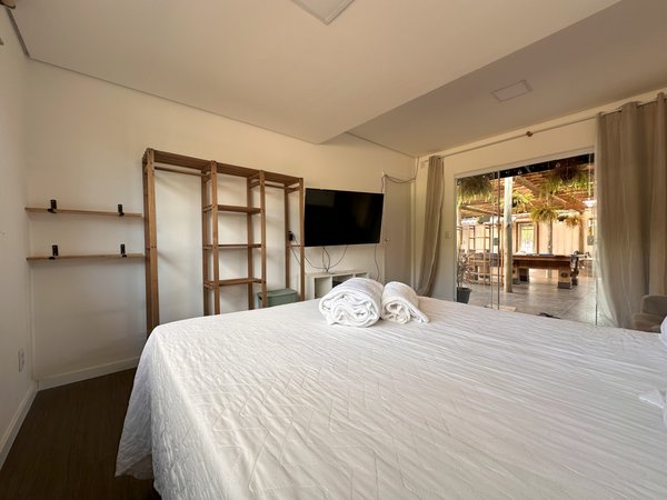 Suíte com cama de casal, prateleiras de madeira e porta para a área externa